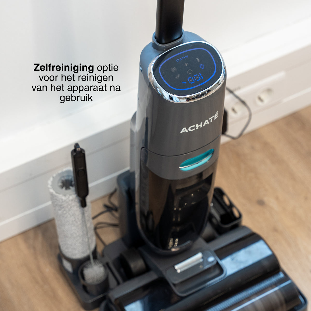 Cordless stick vacuum cleaner with digital display and accessory brushes on wooden floor next to power outlet for multi-surface cleaning.
