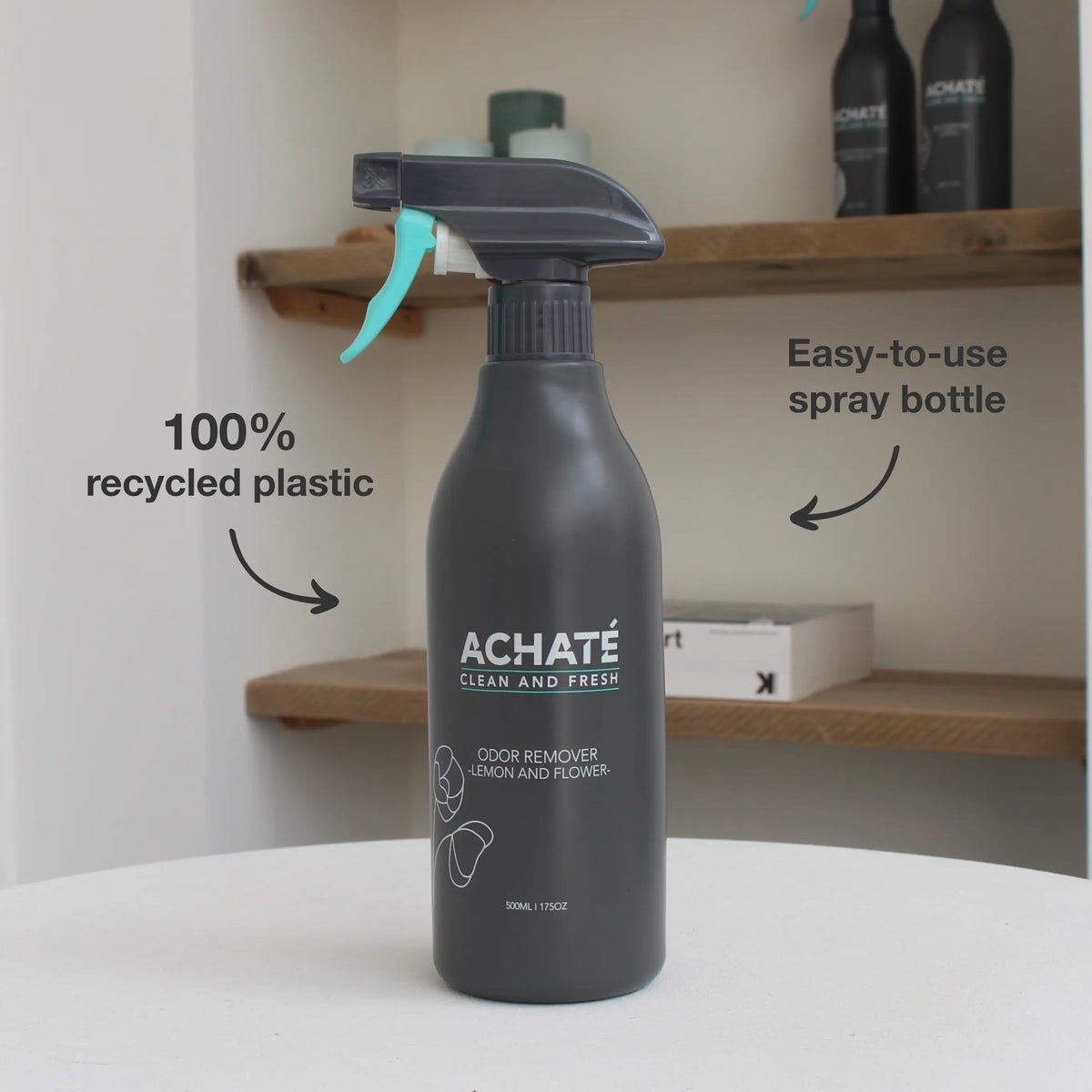 Matte black spray bottle labeled Achaté odor remover with lemon and flower scent, featuring a turquoise spray trigger on a white surface with wooden shelves in background.