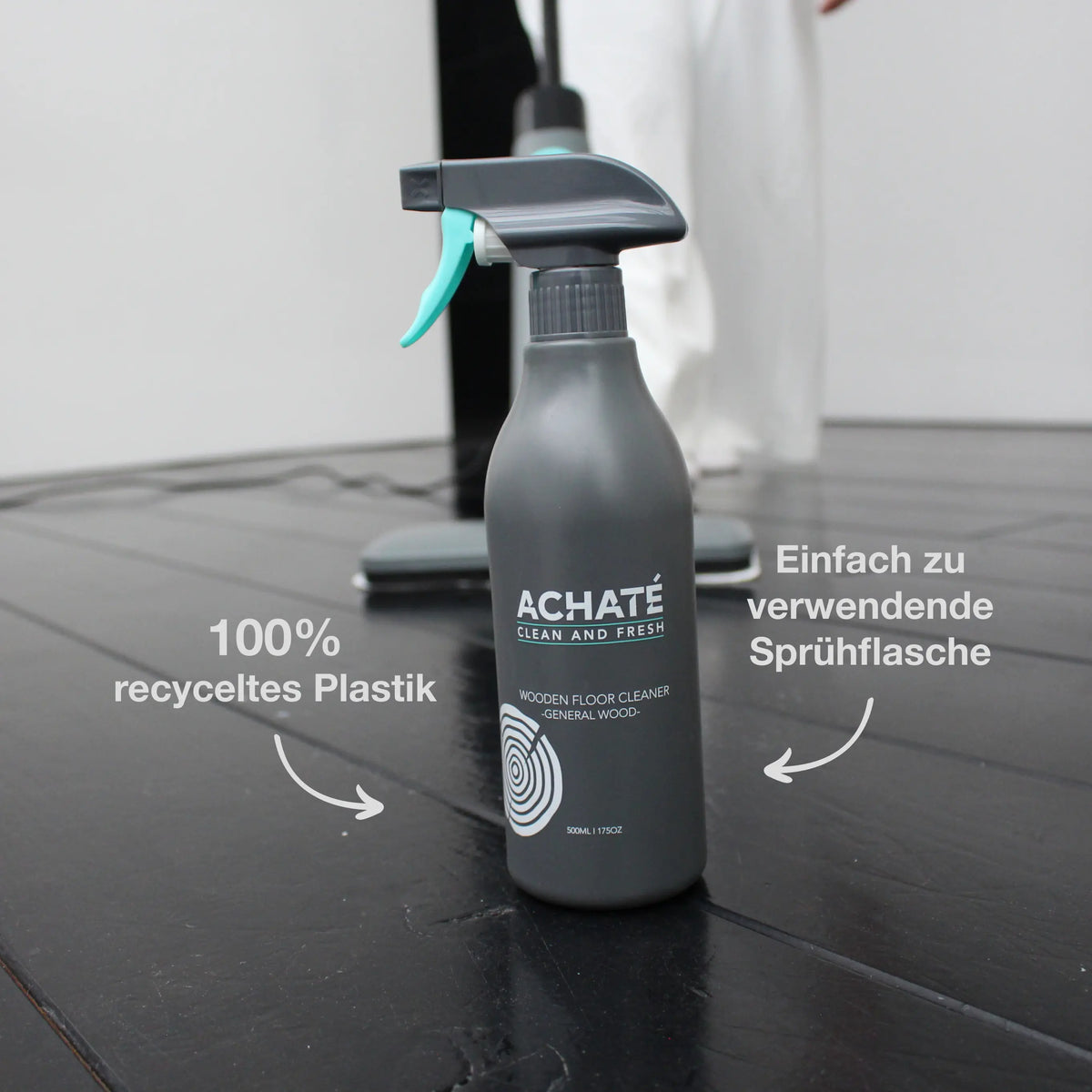 Matte gray spray bottle labeled Achaté for wood floor cleaning, shown on a dark wood floor with text highlighting 100% recycled plastic and easy-to-use spray features.