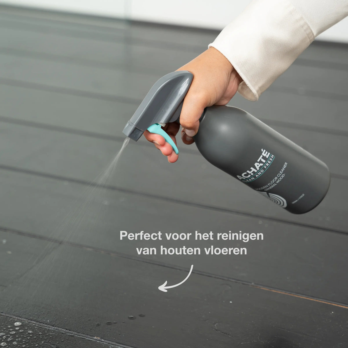 Handheld spray bottle releasing a fine mist onto a dark wooden floor, demonstrating chemical-free cleaning for hardwood surfaces.