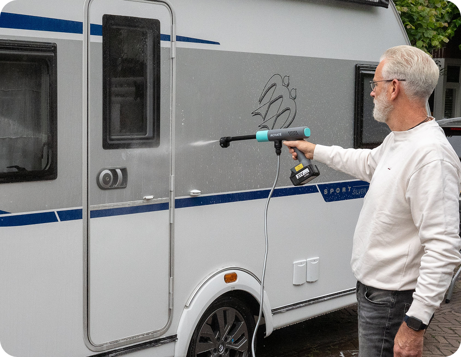 Man using a handheld steam cleaner with high steam pressure to clean the exterior side of a white caravan, demonstrating chemical-free cleaning.