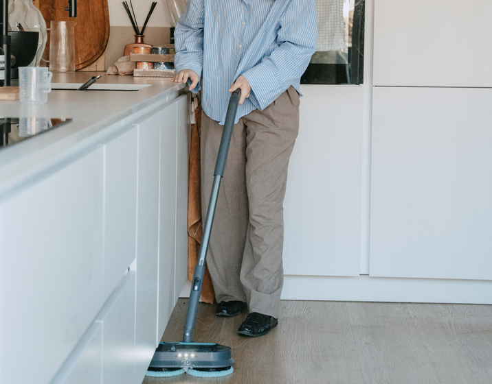 Vrouw reinigt een houten keukenvloer met de Achate elektrische dweil