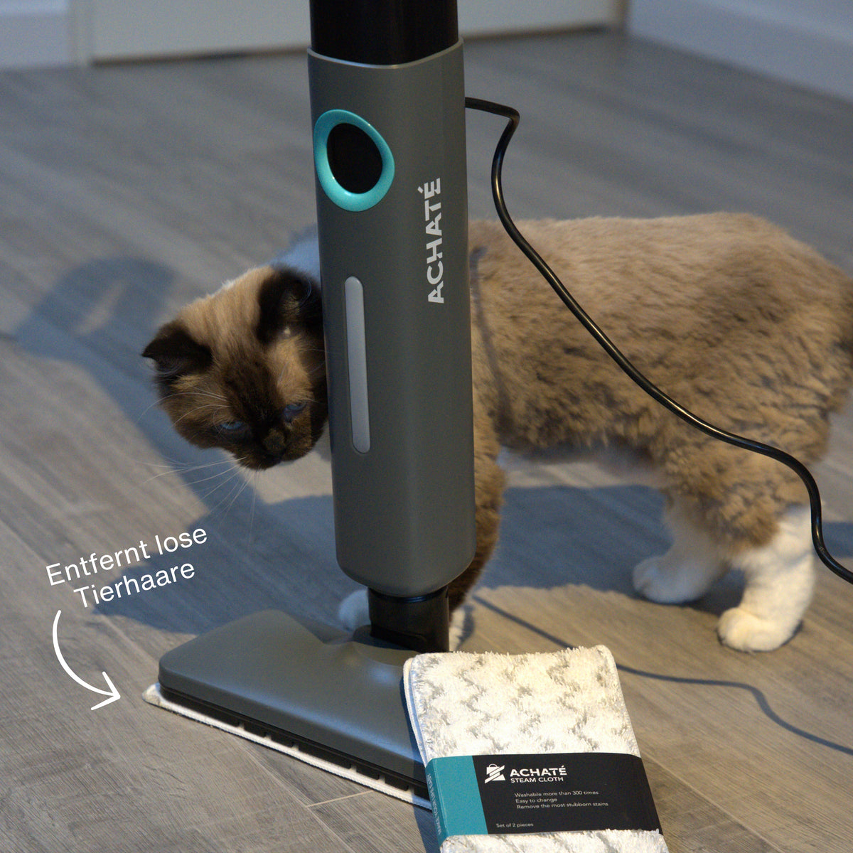 Corded handheld steam cleaner with cleaning pad removing pet hair from hardwood floor next to a curious cat.