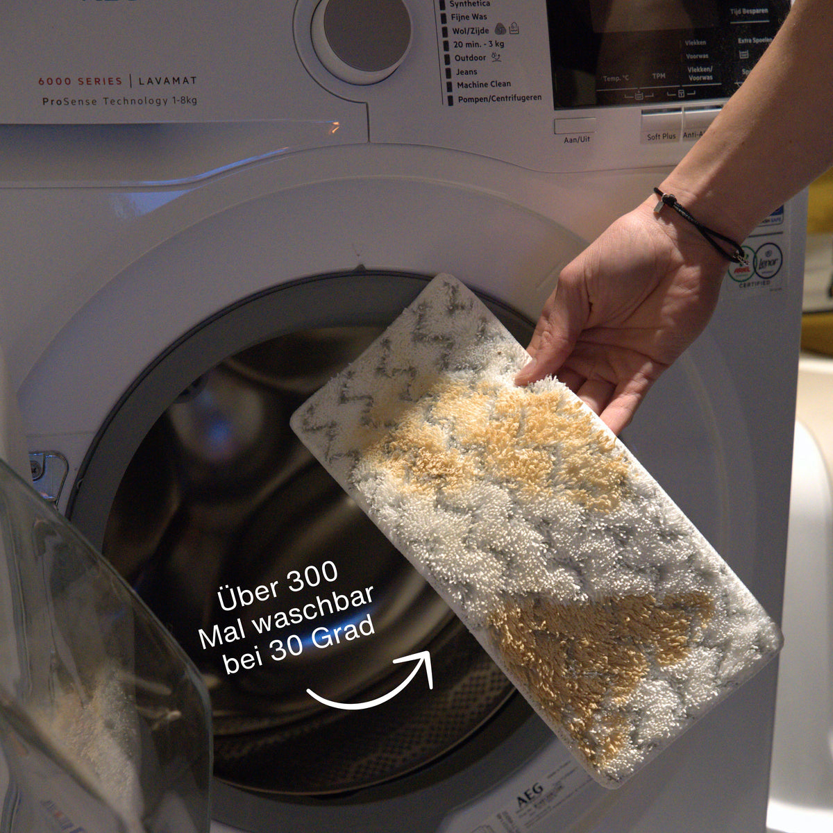 Hand removing a washable rectangular cleaning pad with textured surface from a front-loading washing machine door.