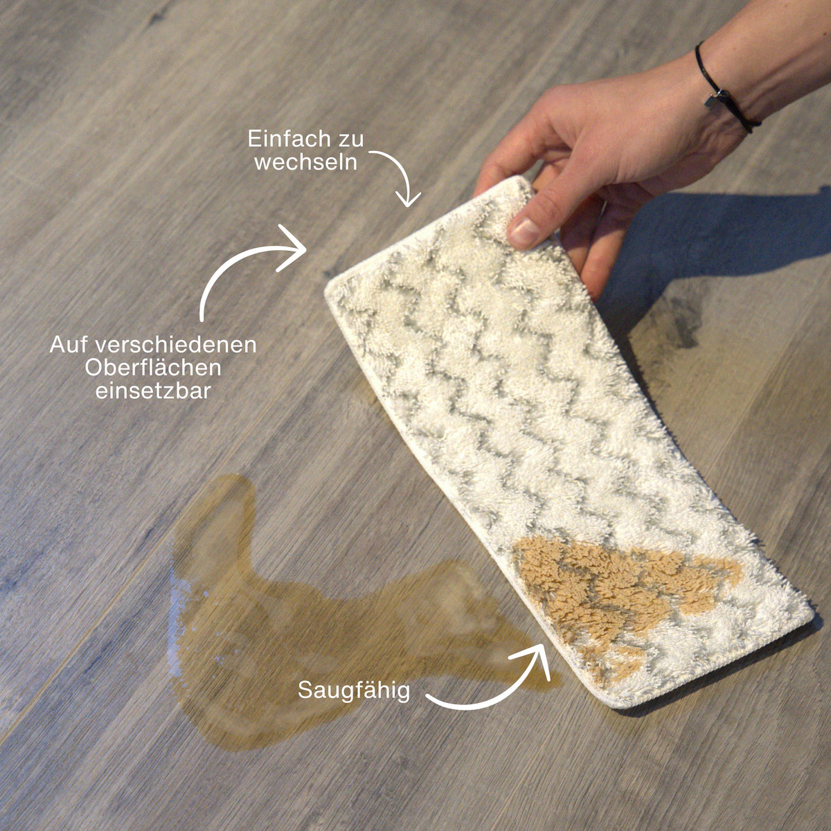 Hand holding an absorbent cleaning pad with visible dirt stains being used on a light wooden floor surface.