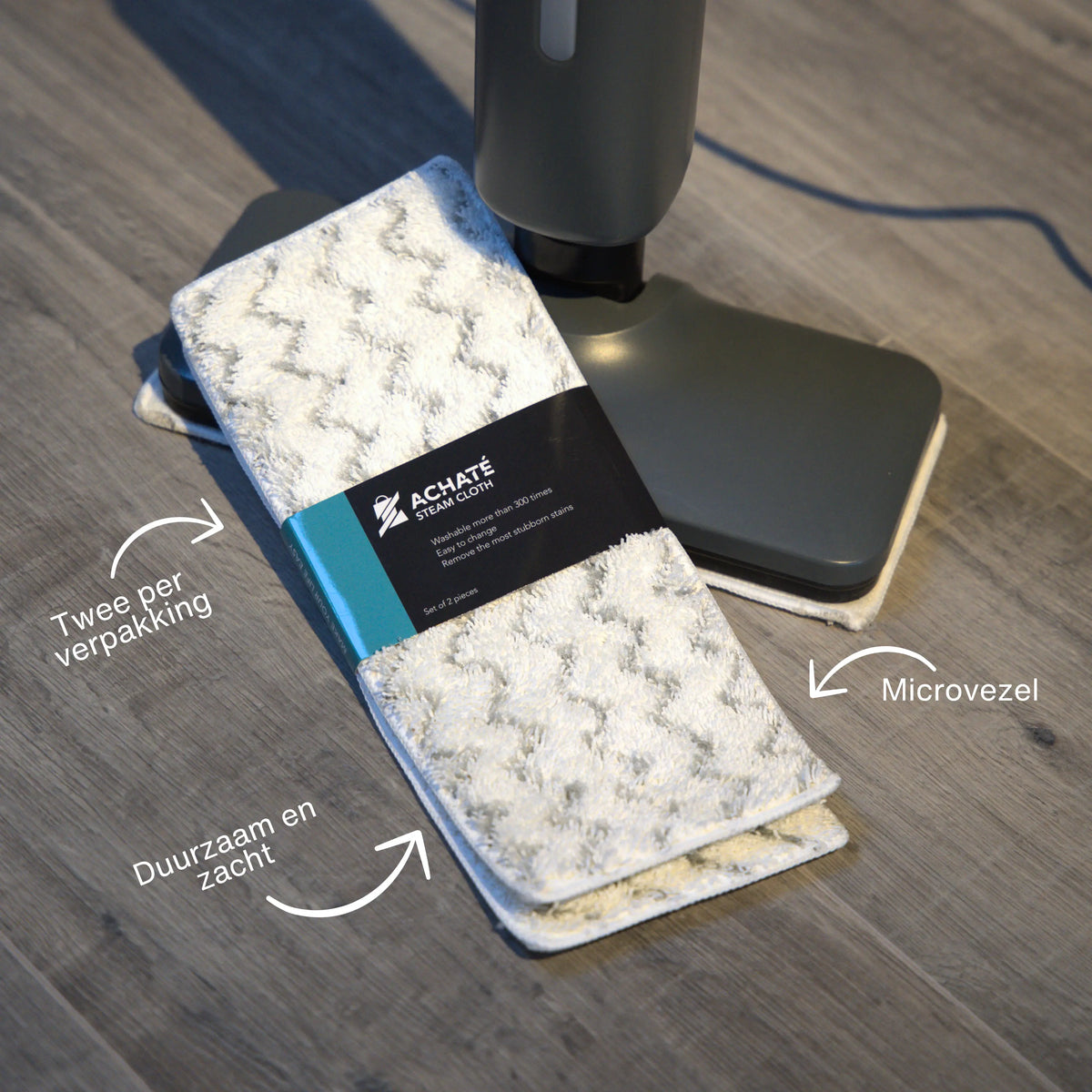 Microfiber steam cloths packaged in pairs with textured surface, placed next to a cordless steam cleaner on a wooden floor.