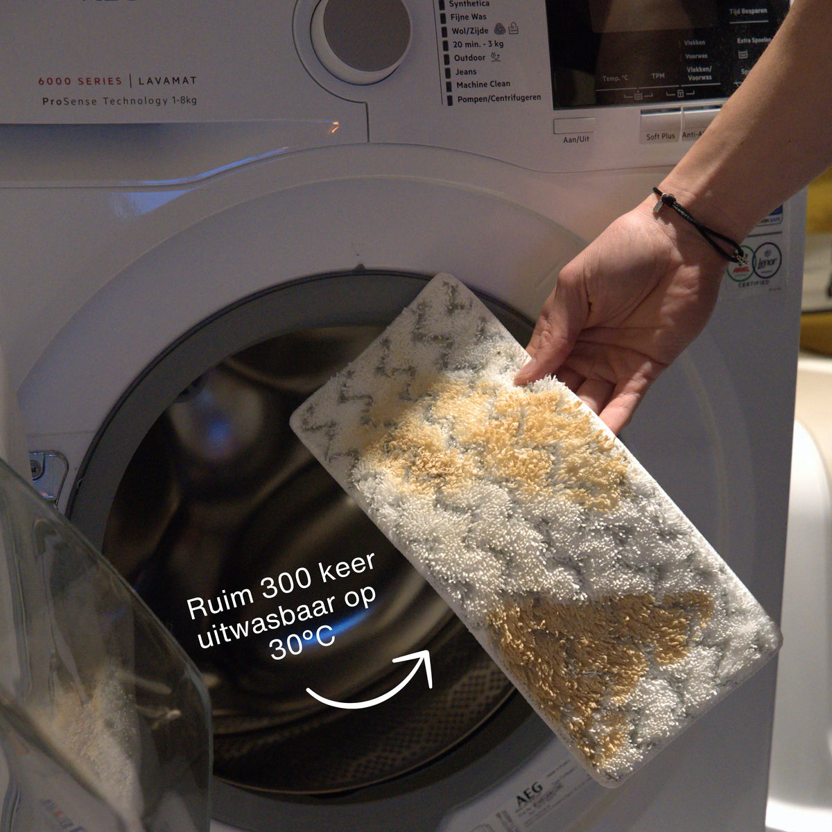 Person removing a washable steam mop pad with beige and white textured fibers from the drum of a front-loading washing machine
