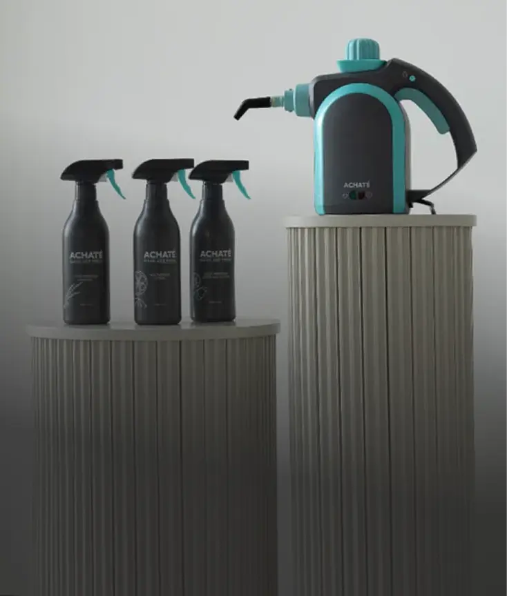 Three Achaté spray cleaners and a teal handheld steam cleaner displayed on ribbed pedestals.