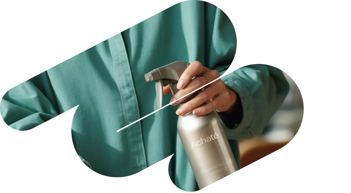 Person wearing a teal shirt holding a silver spray bottle labeled Achaté, against a blurred indoor background.