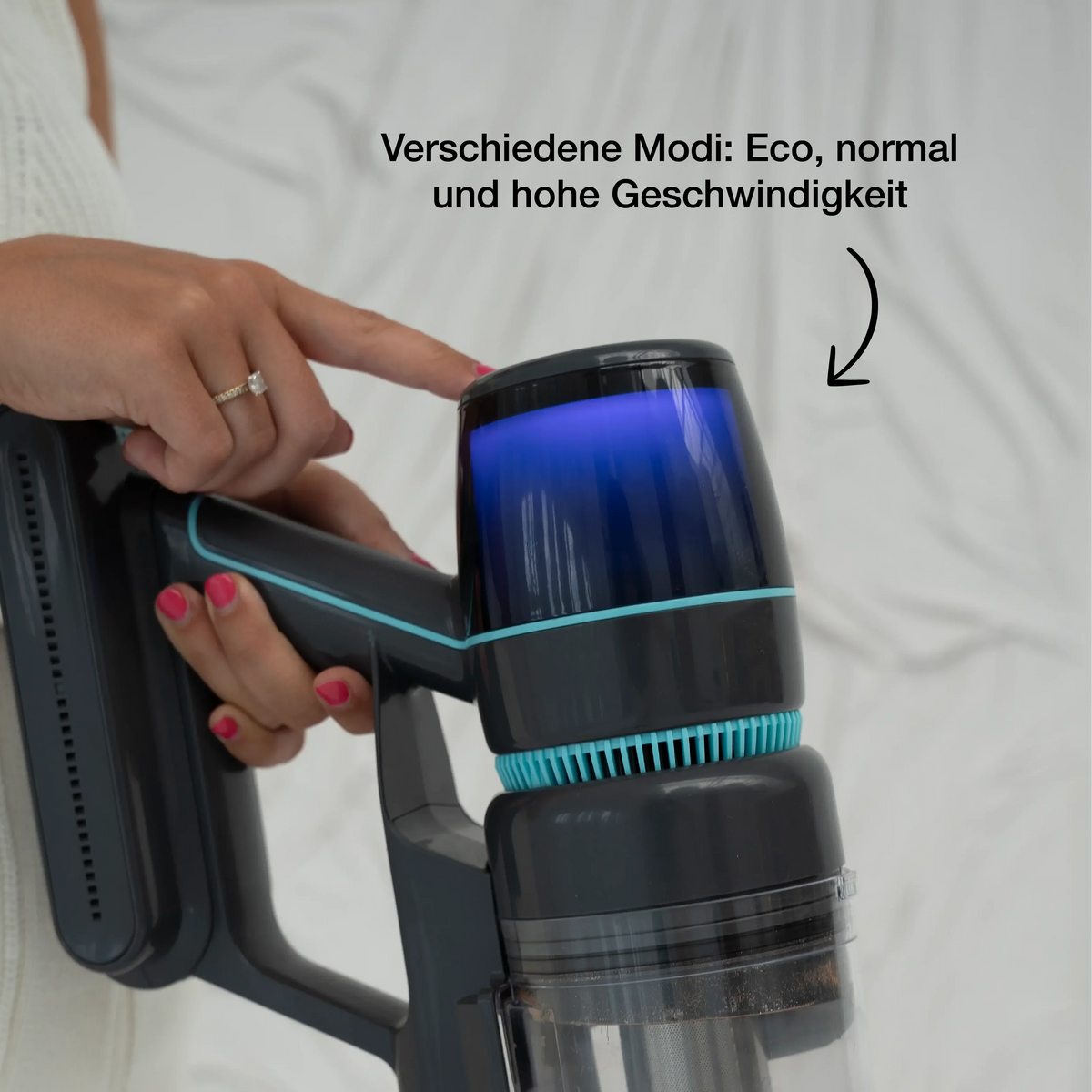 Person adjusting the speed mode button on a sleek black and blue cordless stick vacuum cleaner with visible dust inside the transparent dust container.